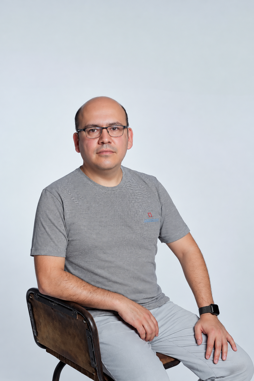 Portrait of Sanjar Mavlyanov seated in a grey t-shirt against a pale studio backdrop